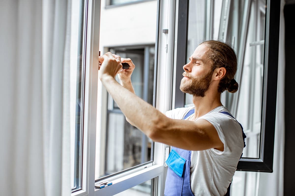 Worker installing and adjusting plastic window frames in a living room